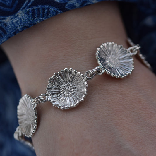 Engraved silver Daisy chain bracelet on the wrist of a girl wearing a blue dress.