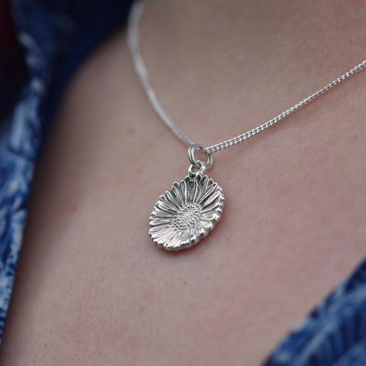 Beautiful shiny intricately detailed Daisy pendant hanging on a silver chain worn by a girl with a blue dress